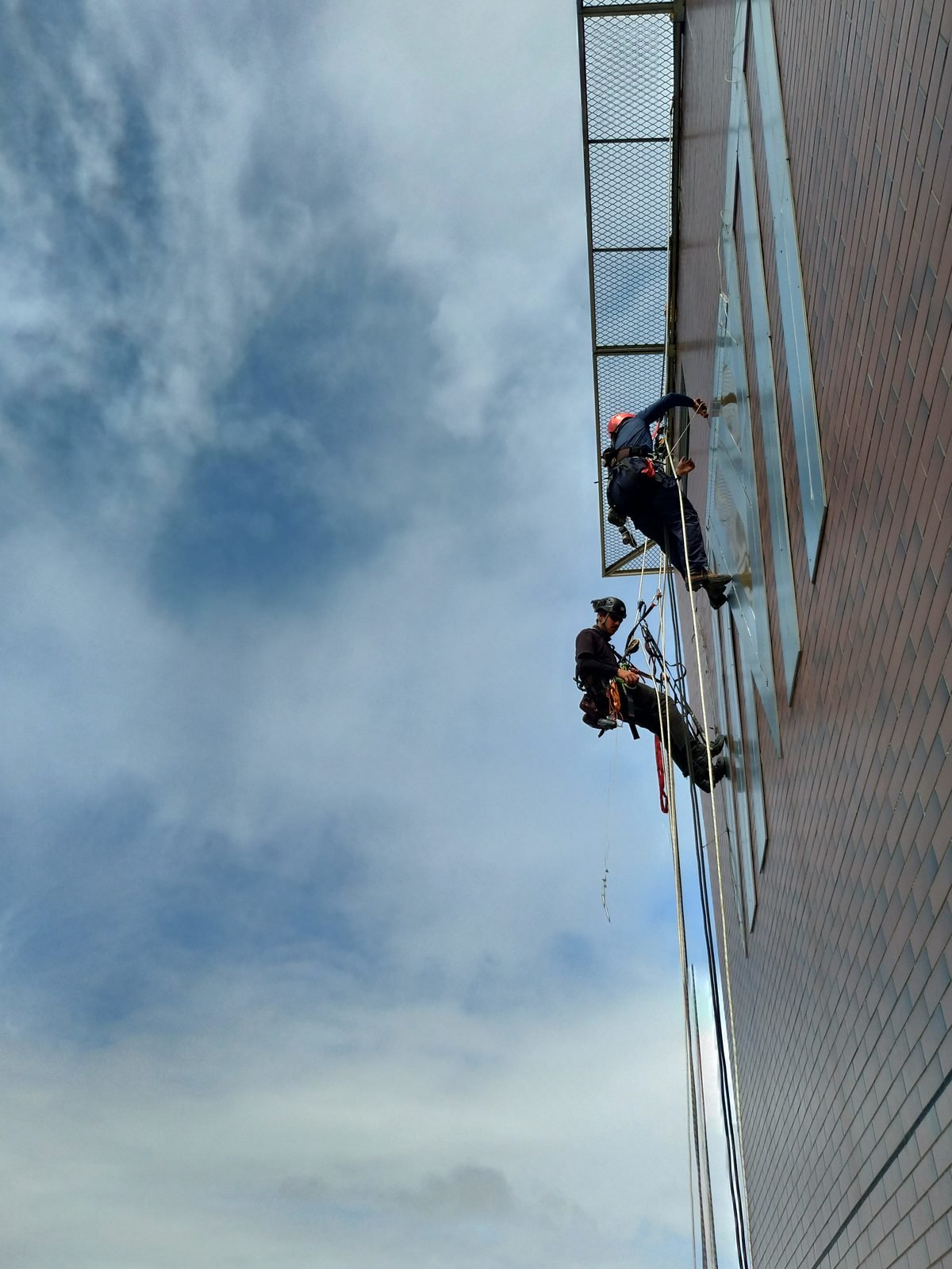 Dois profissionais trabalhando suspensos na fachada de um edifício alto
